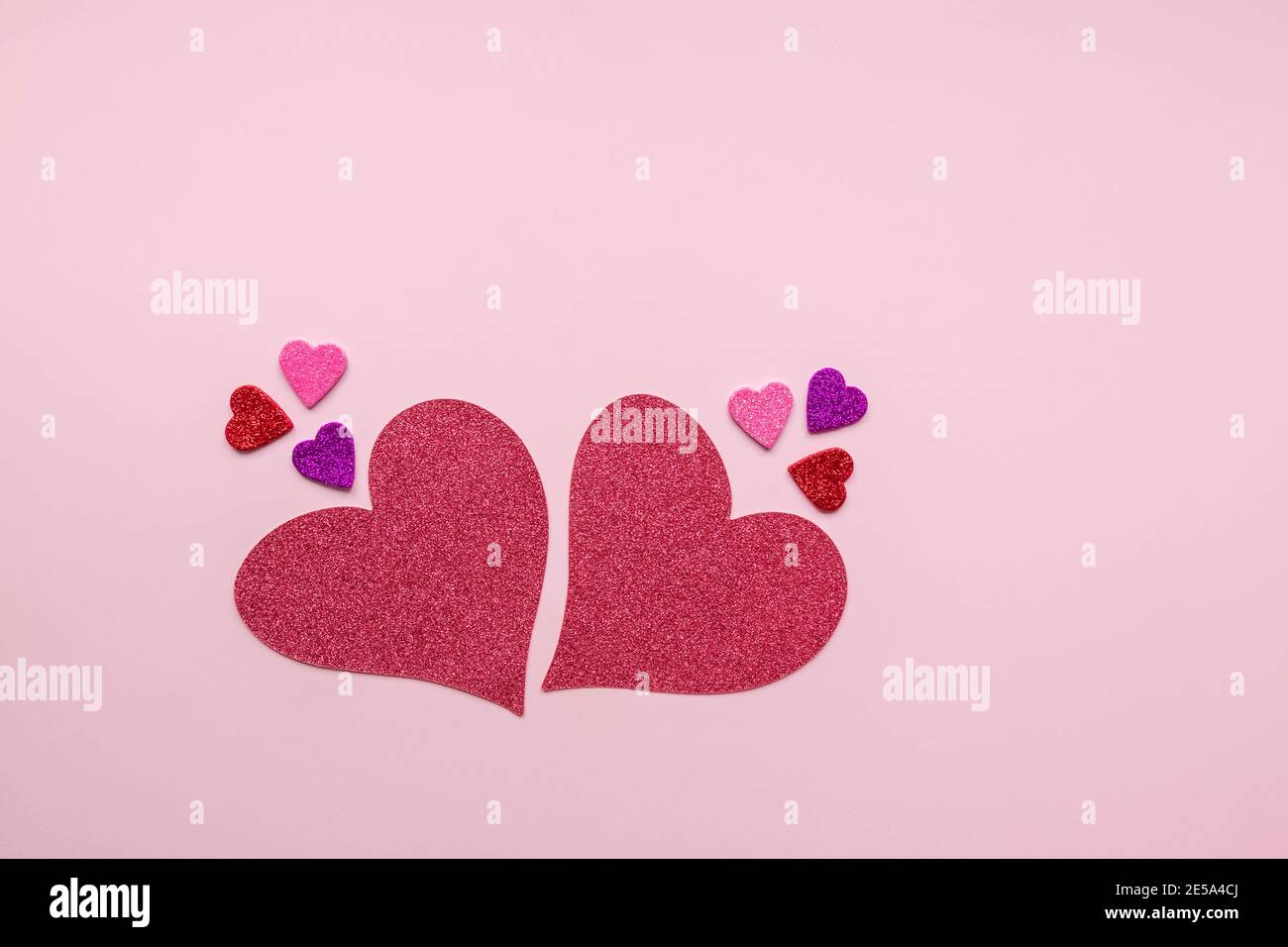 Gros et petit coeurs de papier rouge, rose, violet et violet isolés sur fond rose avec espace de copie. Décoration pour la Saint-Valentin. Pose à plat. Banque D'Images