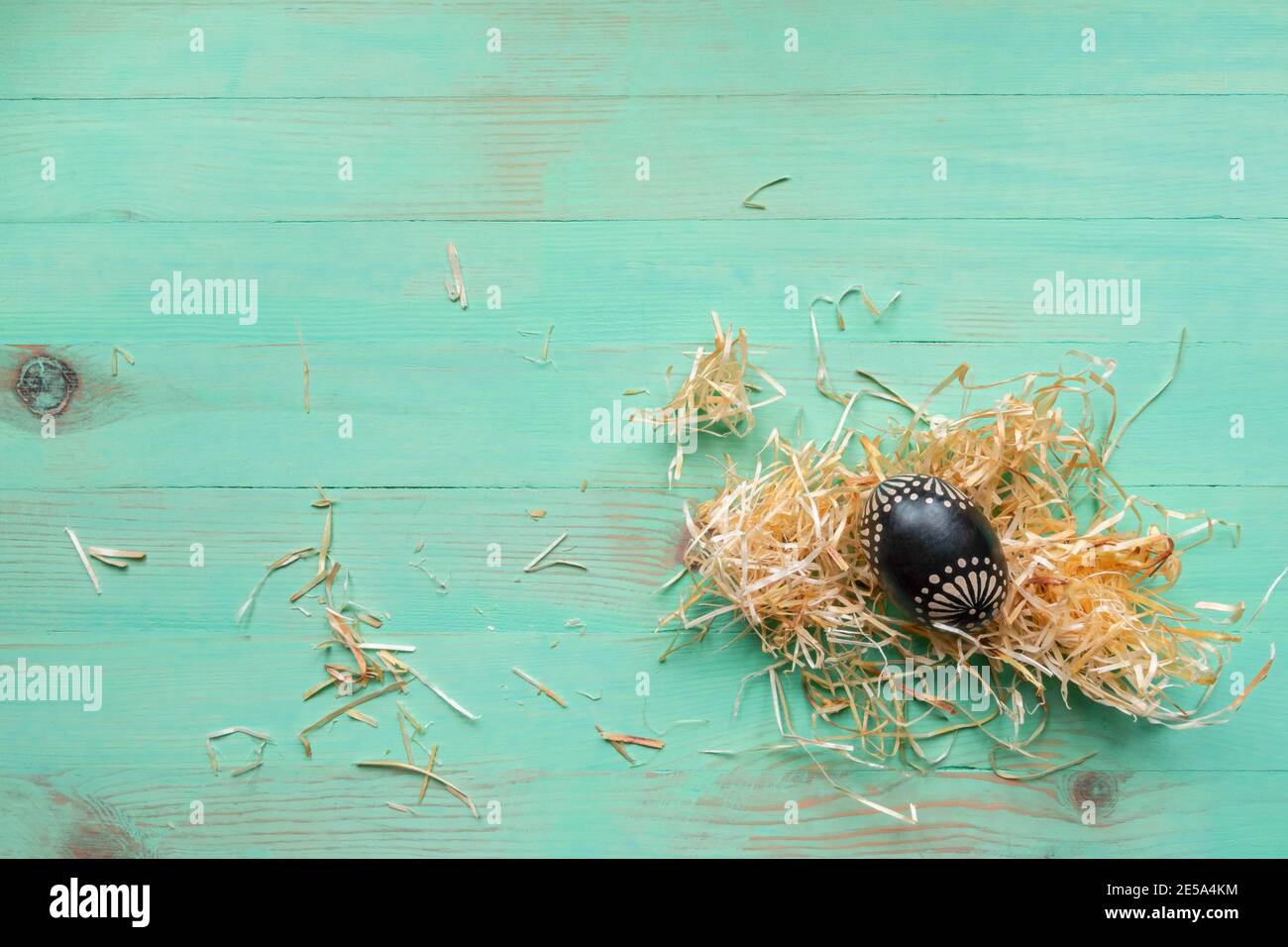 Oeuf de Pâques en bois peint en noir avec pailles de foin sur fond de bois vert clair vintage. Concept de Pâques de style rustique. Vue de dessus. Plat Banque D'Images