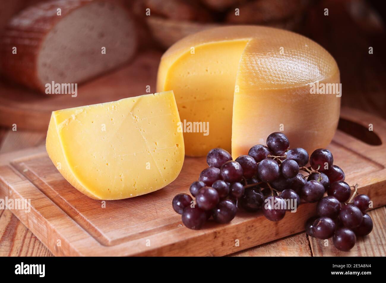 pain jaune de fromage dur sur une planche à découper, raisins, encore la vie Banque D'Images