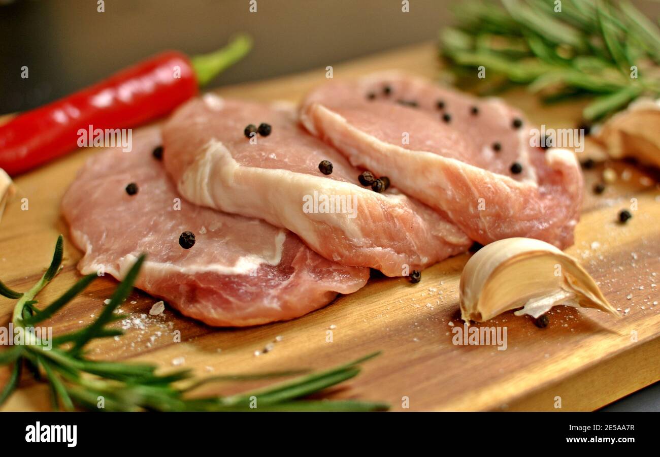 Plat de filet de viande de porc frais non cuite, cru, au romarin, au poivre, au piment rouge, à l'ail sur une planche de bois Banque D'Images