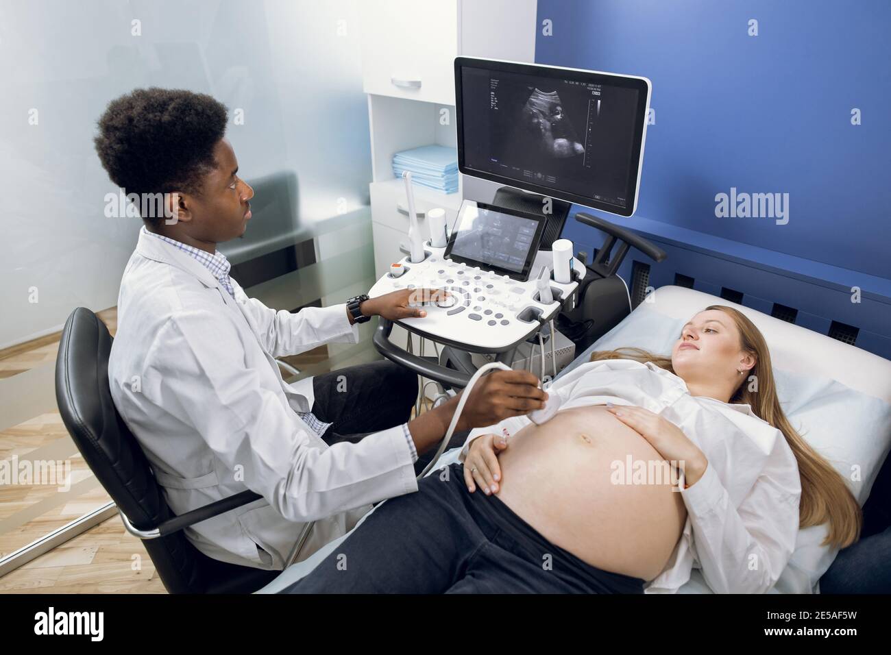 Test échographique. Grossesse. Vue d'angle supérieure du jeune homme  africain médecin gynécologue prof échographie de dépistage pour sa jeune  femme enceinte Photo Stock - Alamy