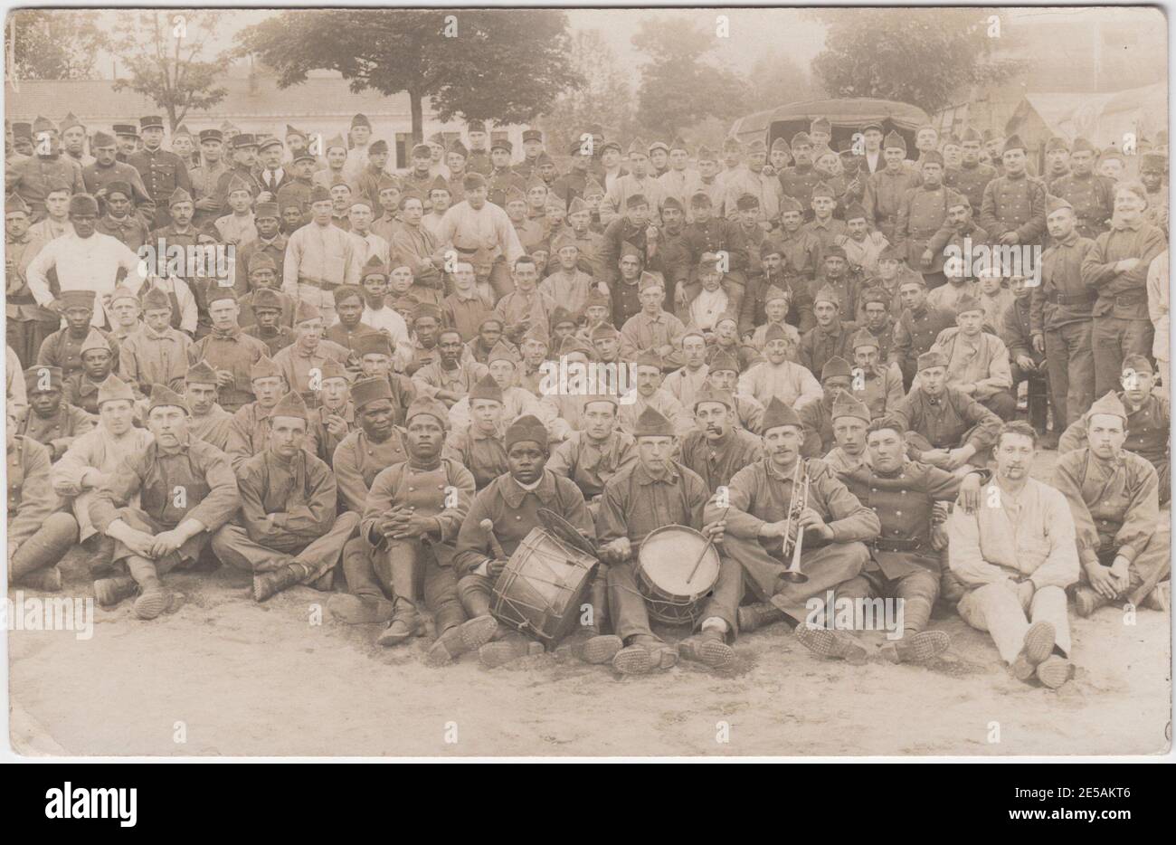Un grand groupe de soldats français et africains réunis en camp pendant la première Guerre mondiale. À l'avant du groupe se trouvent trois hommes (deux blancs, un noir) avec des instruments de musique - une trompette, des tambours et une cymbale Banque D'Images