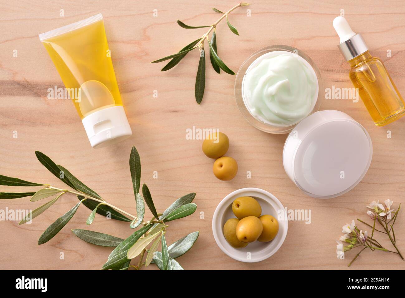 Sérum et crème cosmétique hydratante avec extrait d'olive pour la peau avec branche et olives sur table en bois. Vue de dessus. Banque D'Images