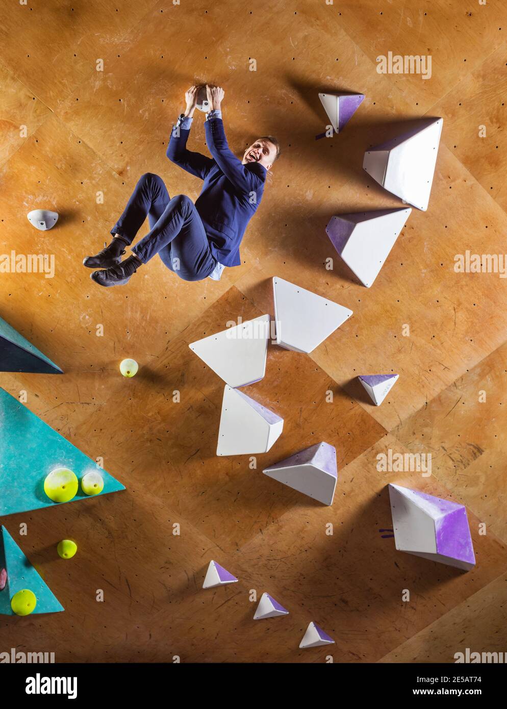 Jeune homme en costume escalade itinéraire difficile sur mur artificiel dans la salle de gym de bloc. Concept de défis de carrière. L'homme d'affaires est heureux qu'il ait la portée Banque D'Images
