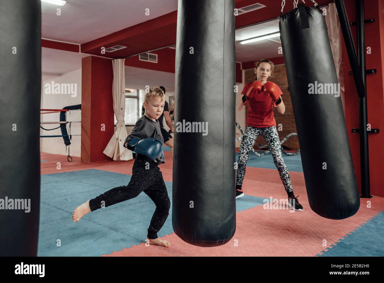 Kickboxing pour enfants dans une salle de sport. Portrait d'une jeune fille et d'un garçon qui donne un coup de pied et poinçonné à un entraînement de boîte de kick dans un club sportif. Banque D'Images
