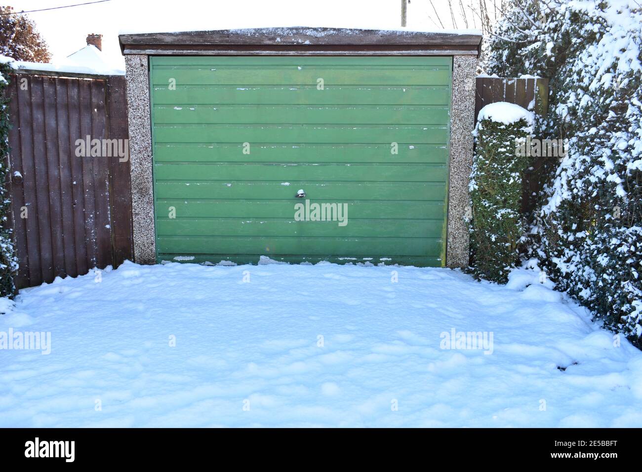 vue rapprochée de l'allée menant à une porte de garage en bois marron couverte de neige profonde bordée d'escrime en bois et d'arbres. à l'extérieur par une journée hivernale Banque D'Images