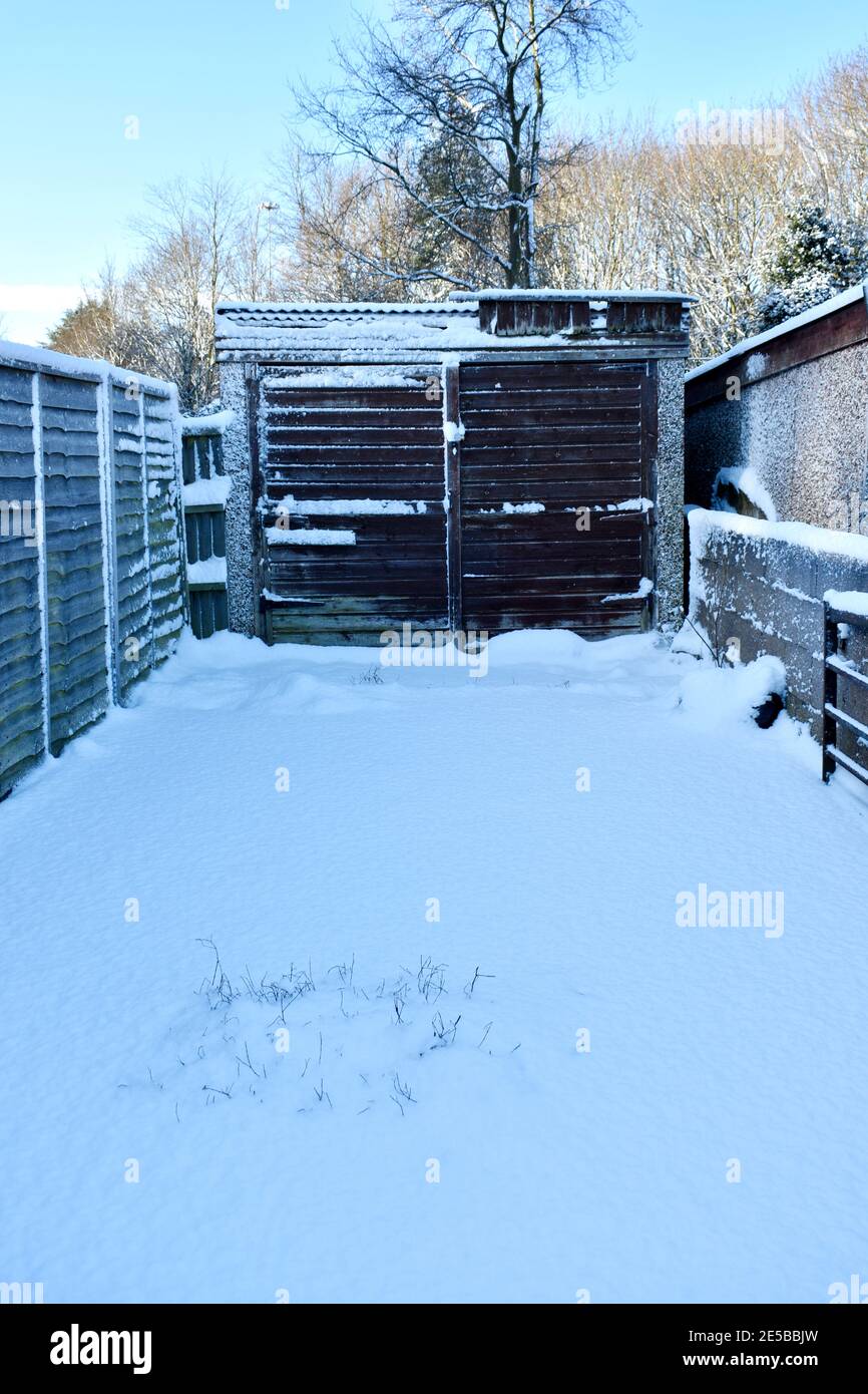 vue rapprochée de l'allée menant à une porte de garage en bois marron couverte de neige profonde bordée d'escrime en bois et d'arbres. à l'extérieur par une journée hivernale Banque D'Images