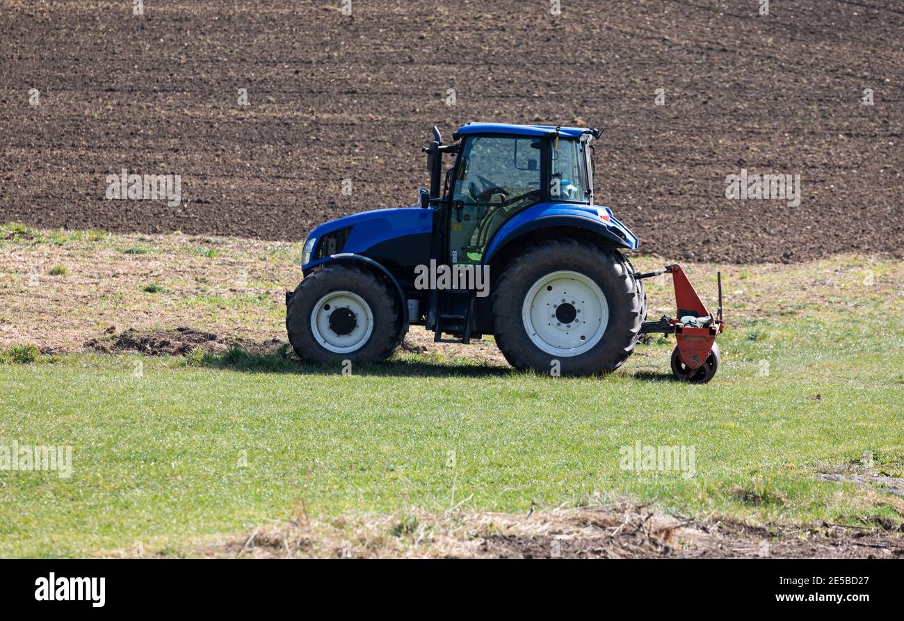 tracteur agricole bleu sans conducteur se tient sur un pré vert devant un champ labouré en arrière-plan, au soleil, pendant la journée Banque D'Images