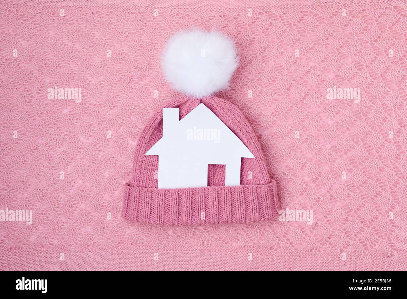 appartement d'hiver avec maison en papier et un chapeau avec pompon sur fond rose. Banque D'Images