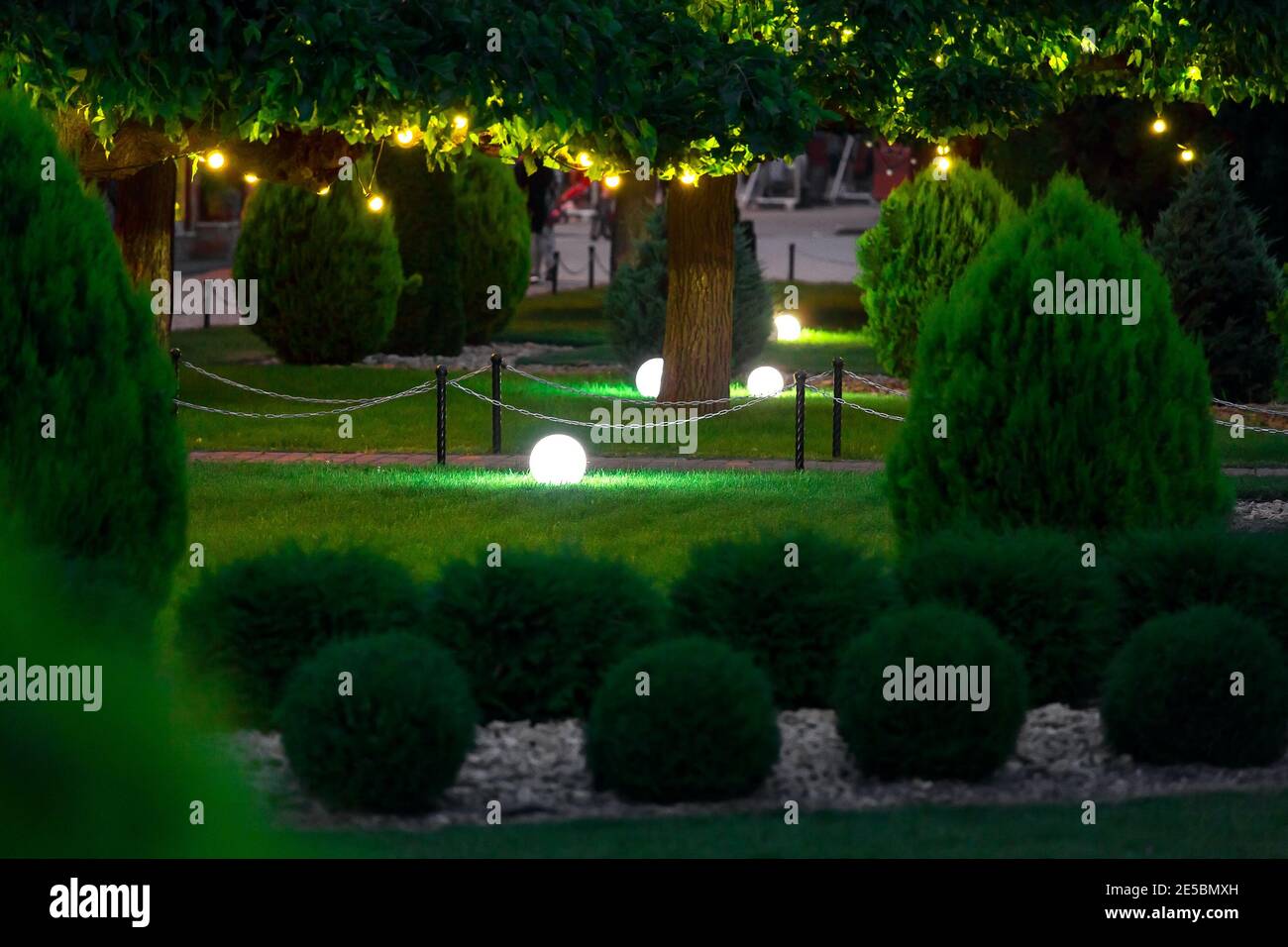 eclairage de jardin avec lanterne électrique à masse et diffuseur à billes lampe sur pelouse avec guirlande d'ampoules chaudes allumée branches d'arbre avec feuilles l Banque D'Images