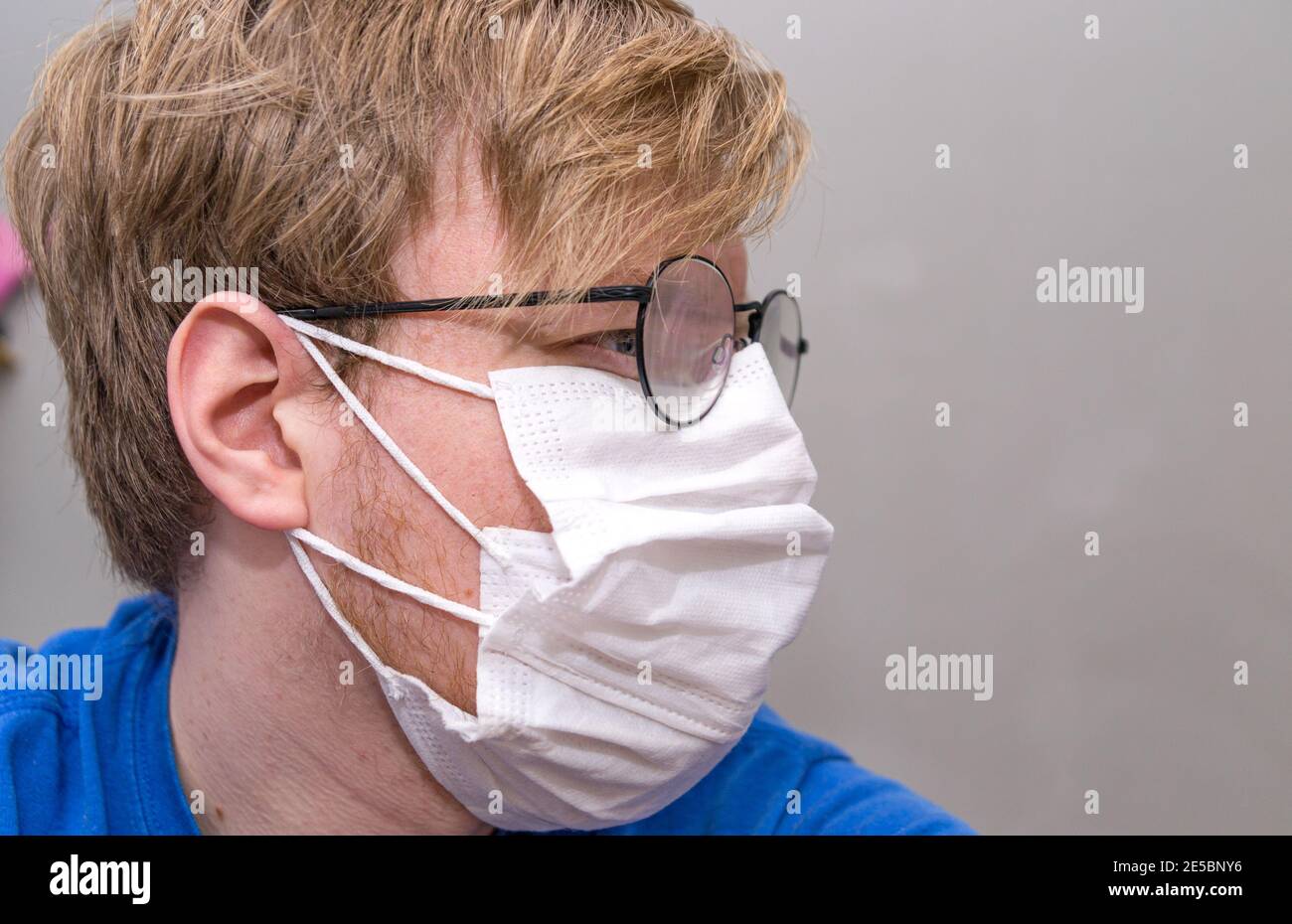 Homme portant deux masques blancs pour la prévention Covid-19 ; lunettes rondes, blanc mâle, cheveux blond. Vue latérale. Banque D'Images