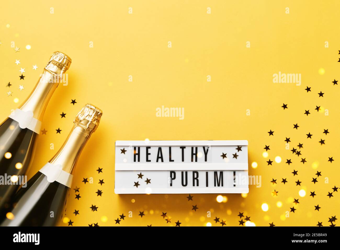 Healthy Purim écrit dans une visionneuse et deux bouteilles de champagne sur fond jaune. Plat de Purim Carnaval Banque D'Images