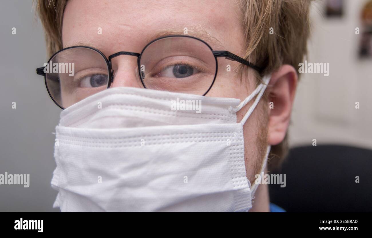 Homme portant deux masques blancs pour la prévention Covid-19 ; lunettes rondes, blanc mâle, cheveux blond. Vue avant. Banque D'Images