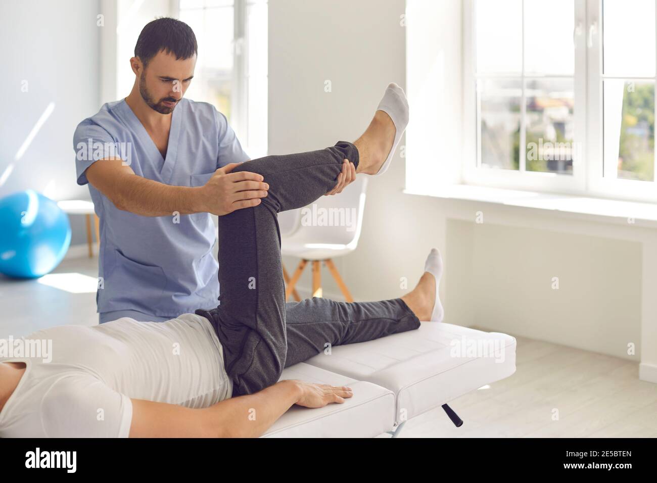 Homme professionnel chiropraticien en bleu uniforme fixation et pose couché homme patients jambes articulations Banque D'Images