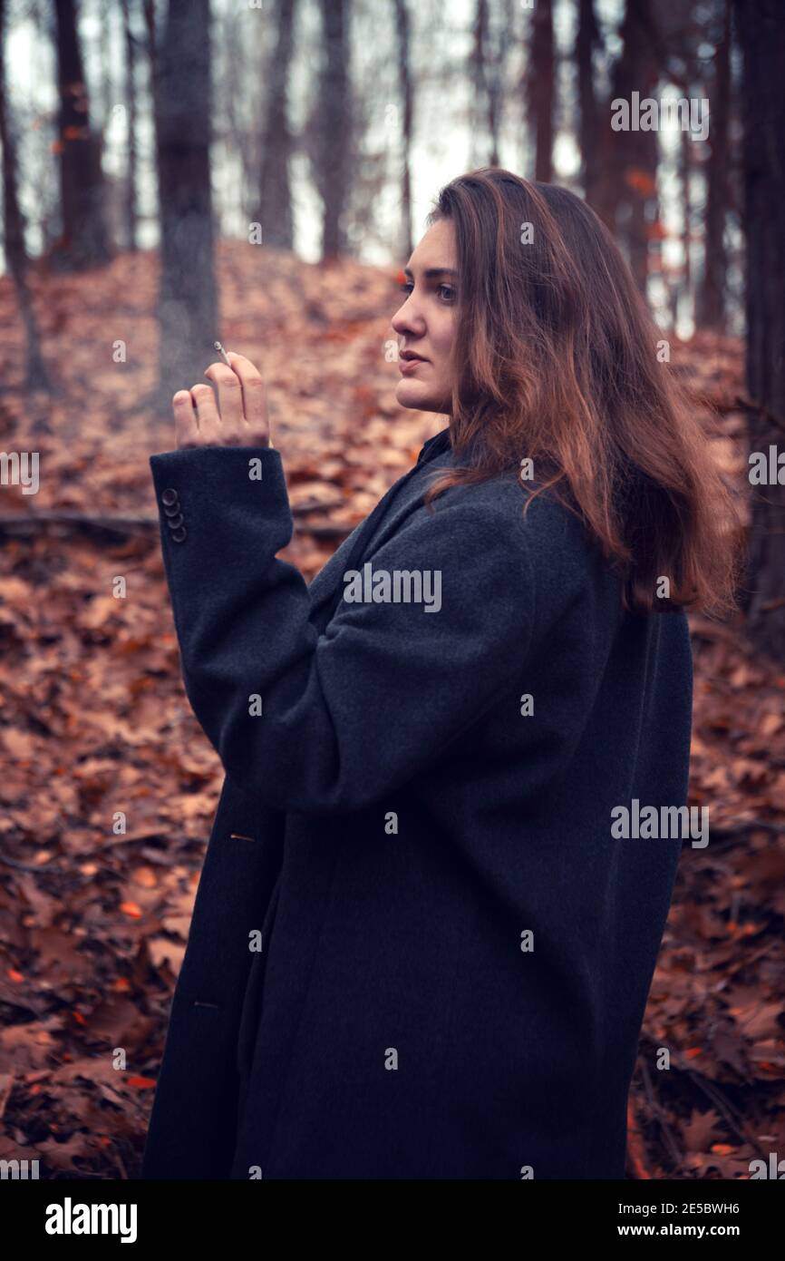 jeune femme brunette fumant de la cigarette dans la forêt en automne Banque D'Images