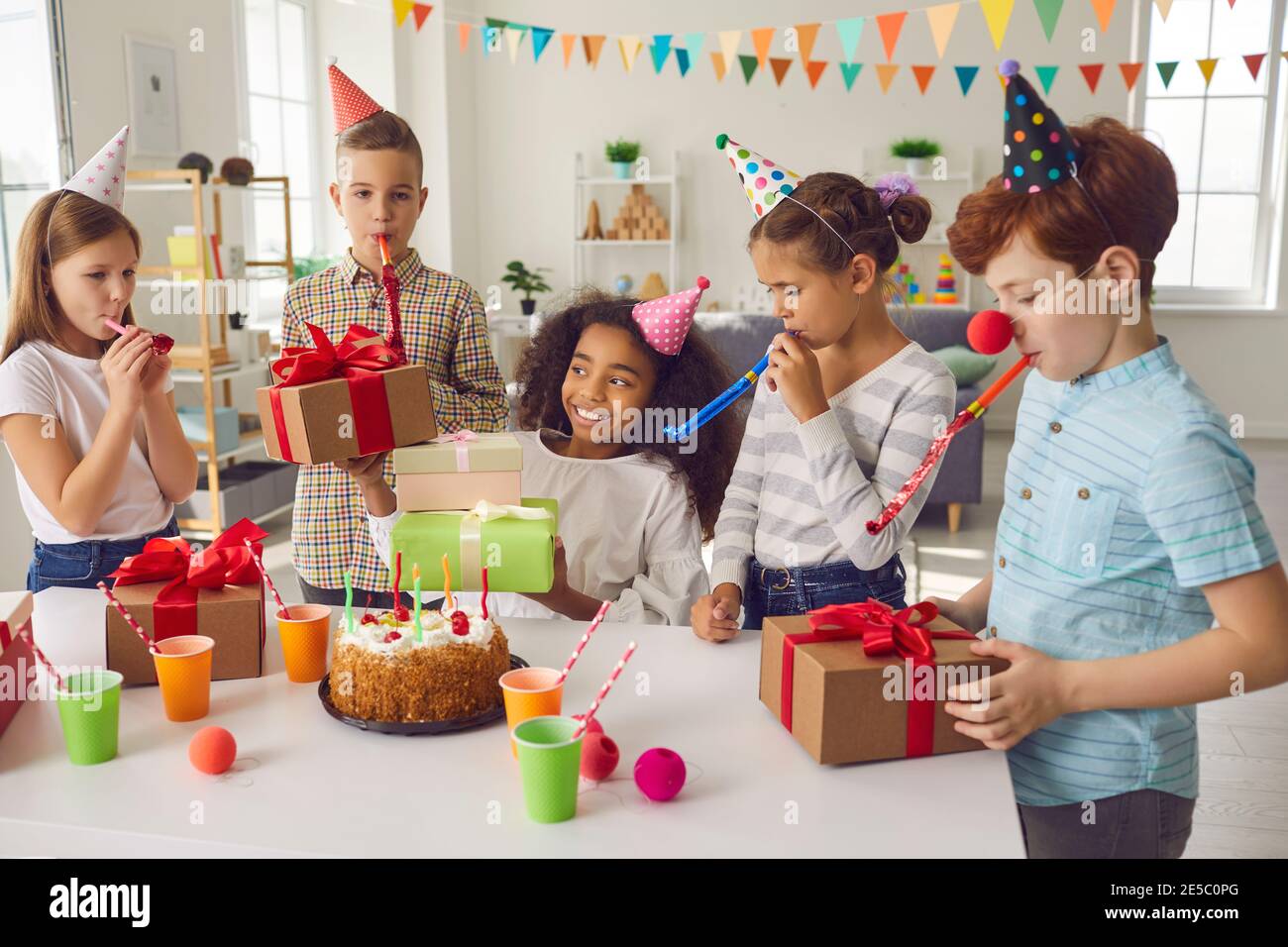 Groupe d'enfants de race mixte souriants avec sifflets décoratifs ayant fête d'anniversaire Banque D'Images