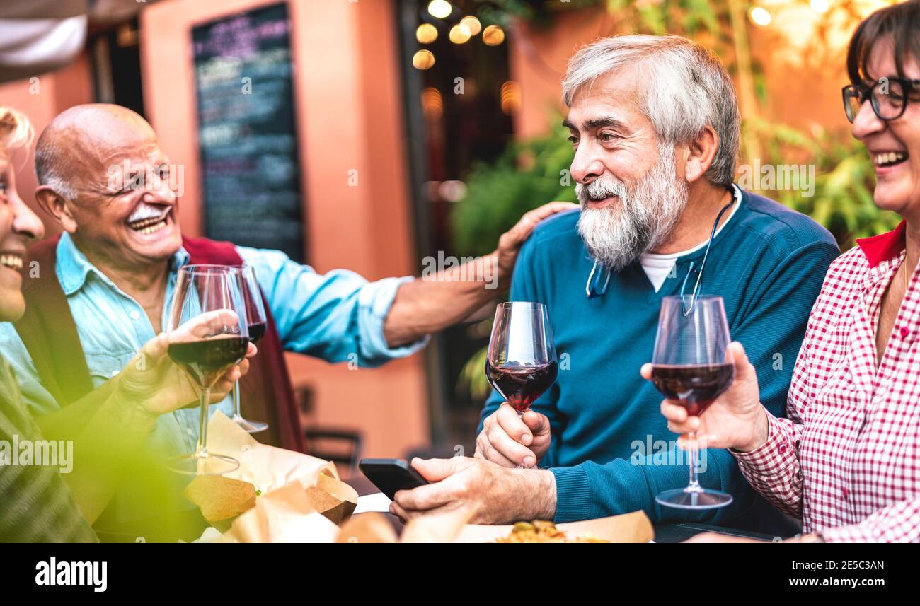 Des amis aînés heureux qui s'amusent à boire du vin rouge au dîner Fête - les gens fatigués mangent au restaurant ensemble - dîner concept de style de vie Banque D'Images