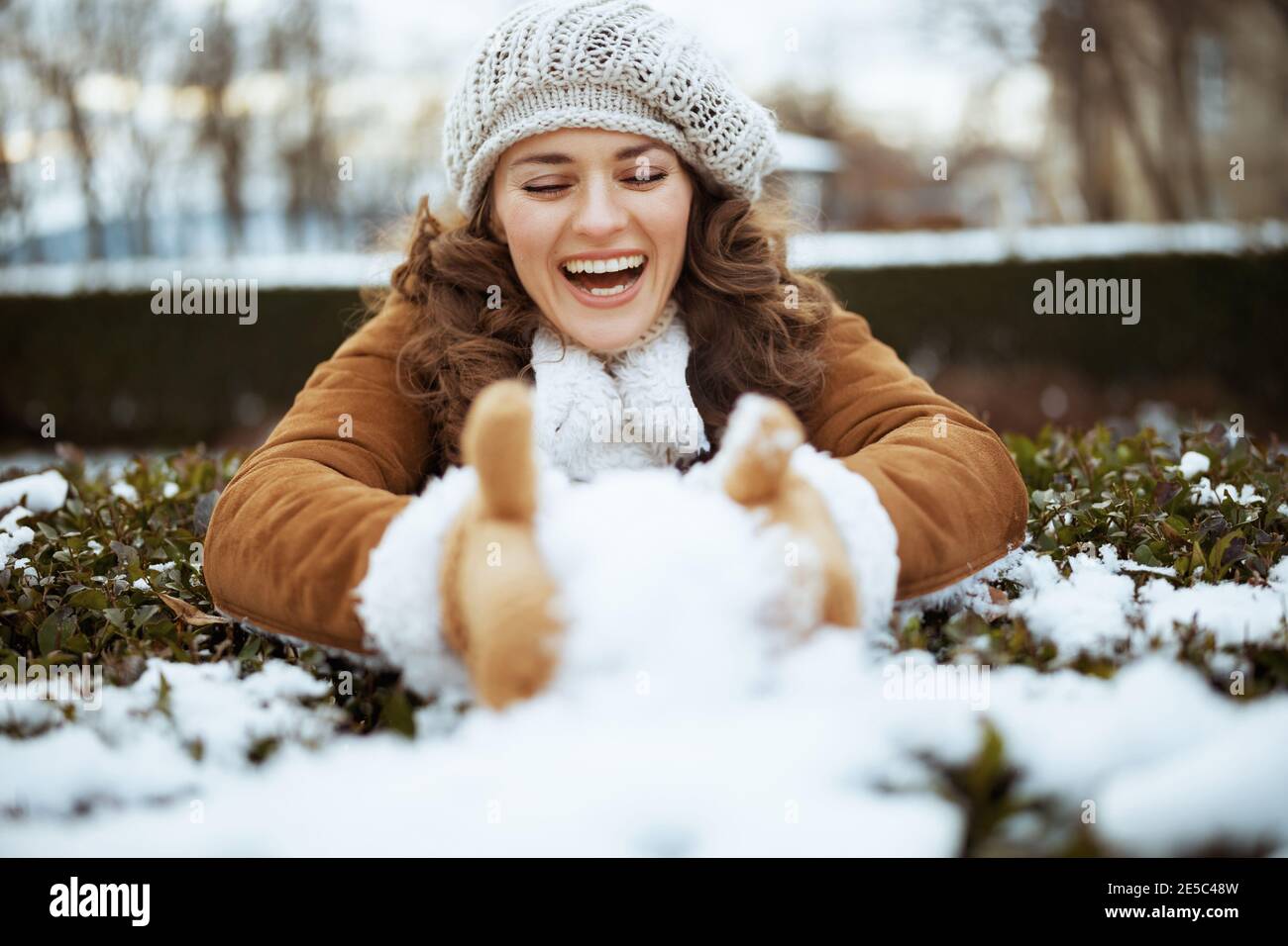 bonne femme moderne de 40 ans avec des moufles dans un bonnet tricoté et un  manteau de peau de mouton jouant à l'extérieur dans le parc de la ville en  hiver Photo