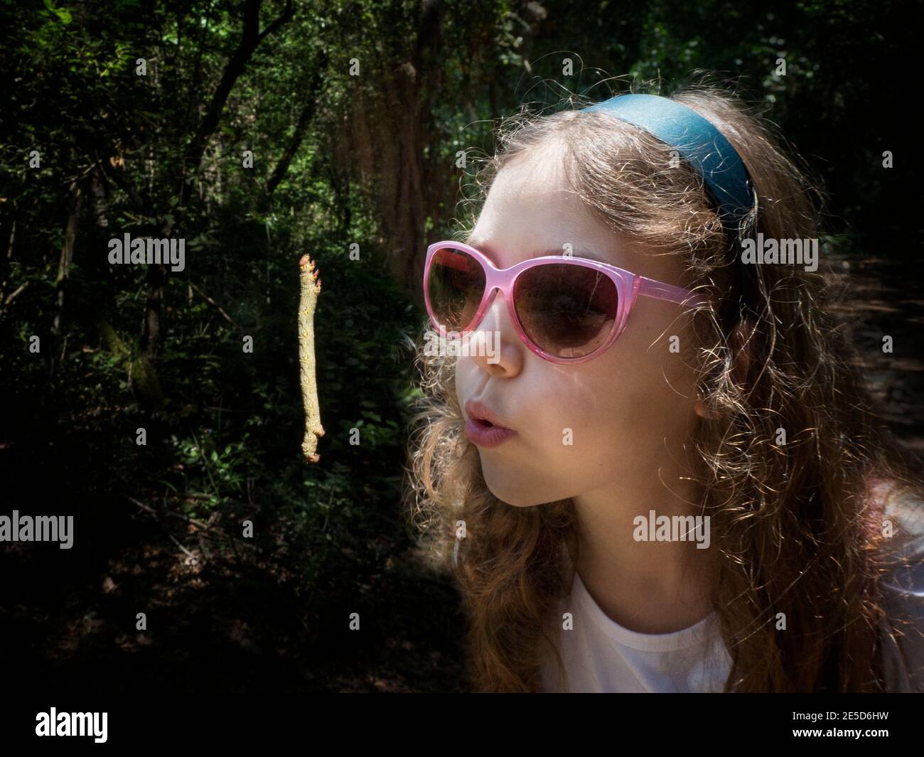 Portrait d'une fille portant des lunettes de soleil soufflant un caterpillar suspendu en plein air, Italie Banque D'Images