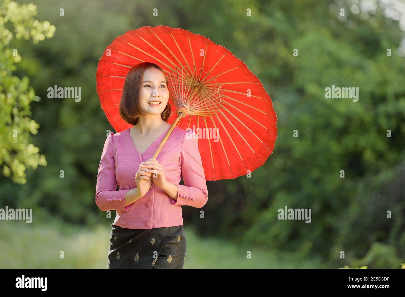 Portrait d'une femme souriante debout dans un jardin tenant un parasol, Thaïlande Banque D'Images