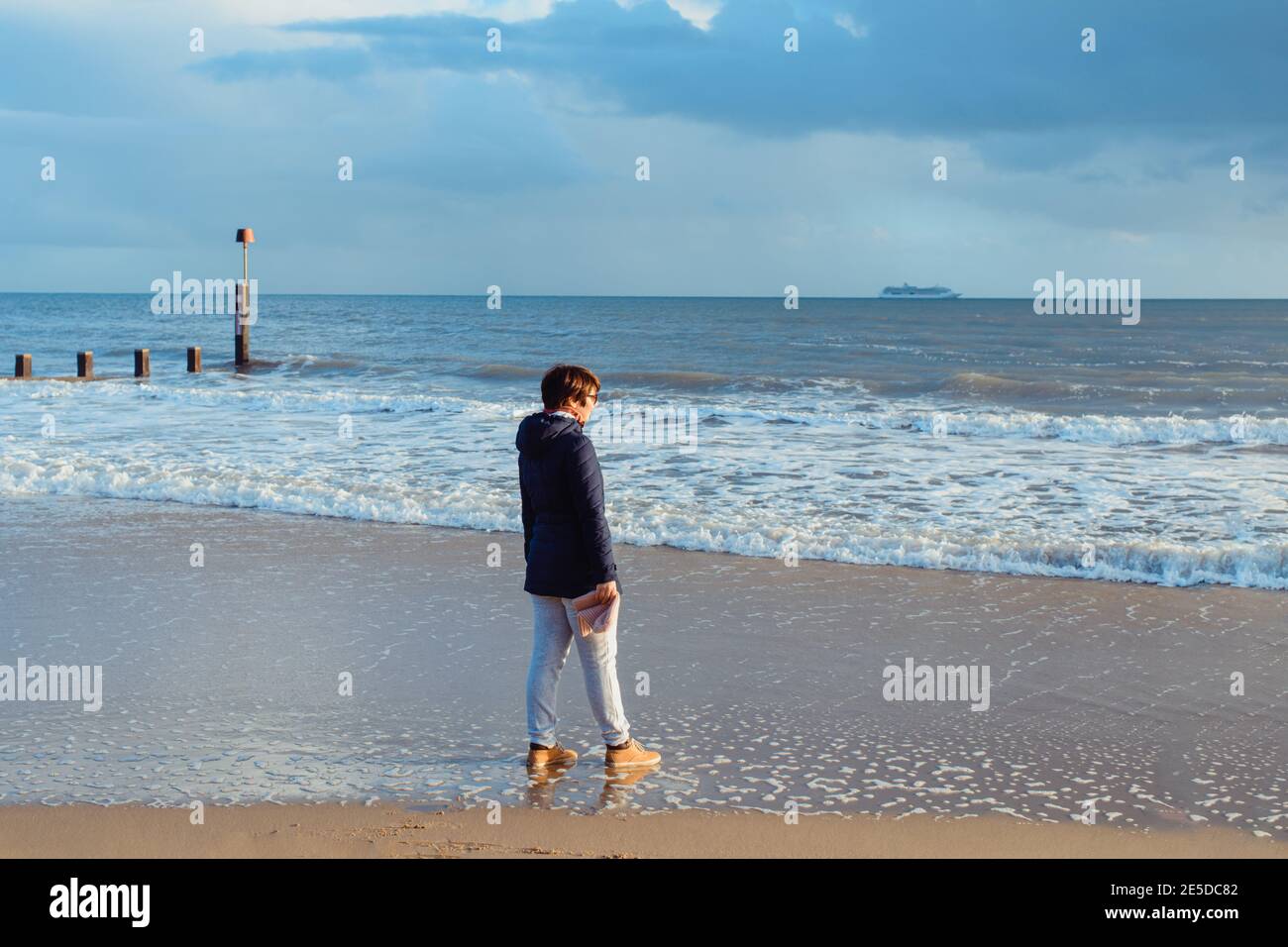 Femme en vêtements chauds et lunettes de soleil appréciant le moment et la vue sur la mer pendant une promenade sur la côte. Détente et accomplissement personnel. Voyagez en automne Banque D'Images