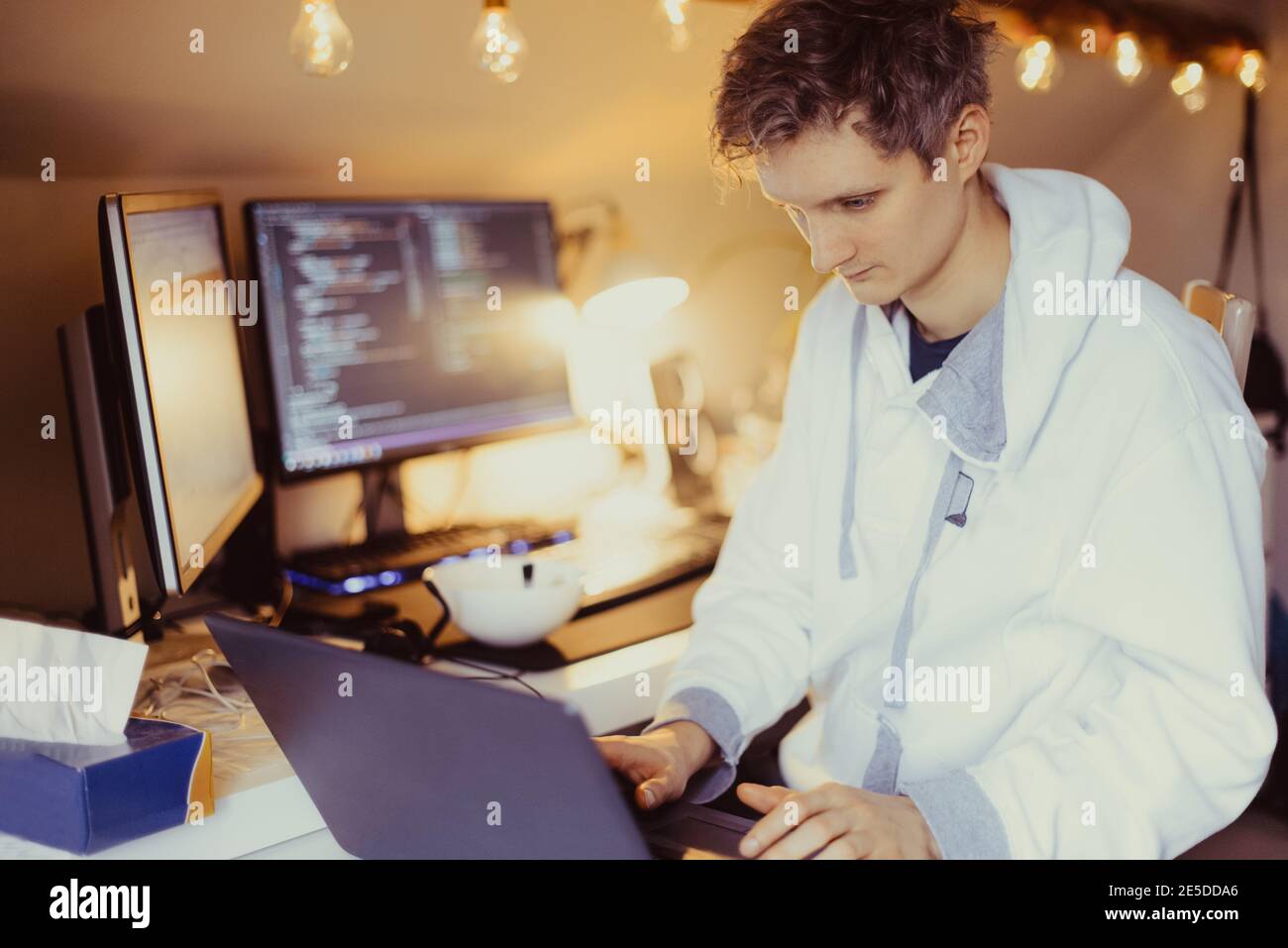 Un homme assis à un bureau travaillant à la maison sur son ordinateur. Un programmeur informatique spécialisé écrit du code sur son pc et son ordinateur portable. Bureau à distance du développeur Banque D'Images