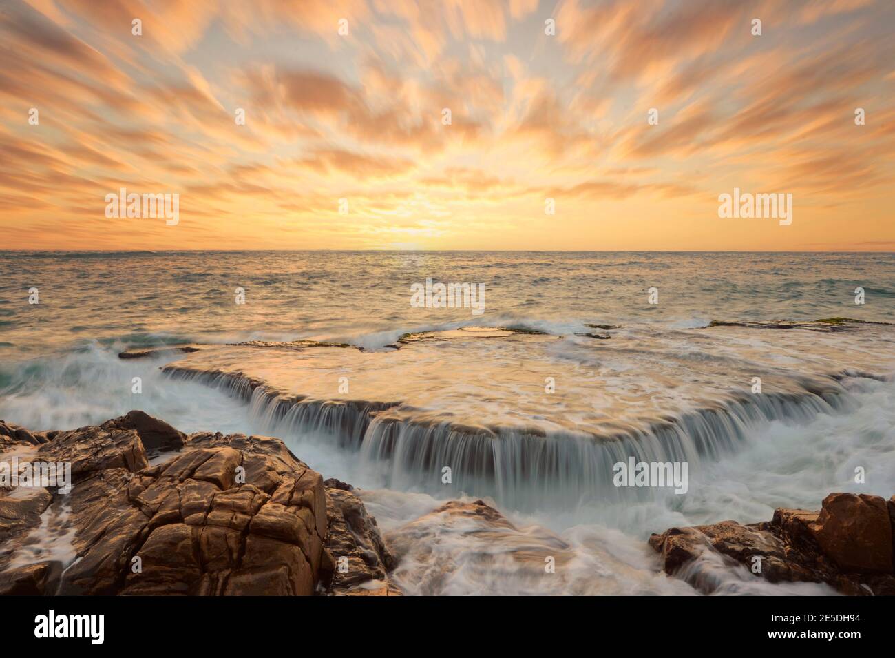 Coucher de soleil sur la côte avec l'océan qui coule au-dessus des rochers, Mui ne, Vietnam Banque D'Images