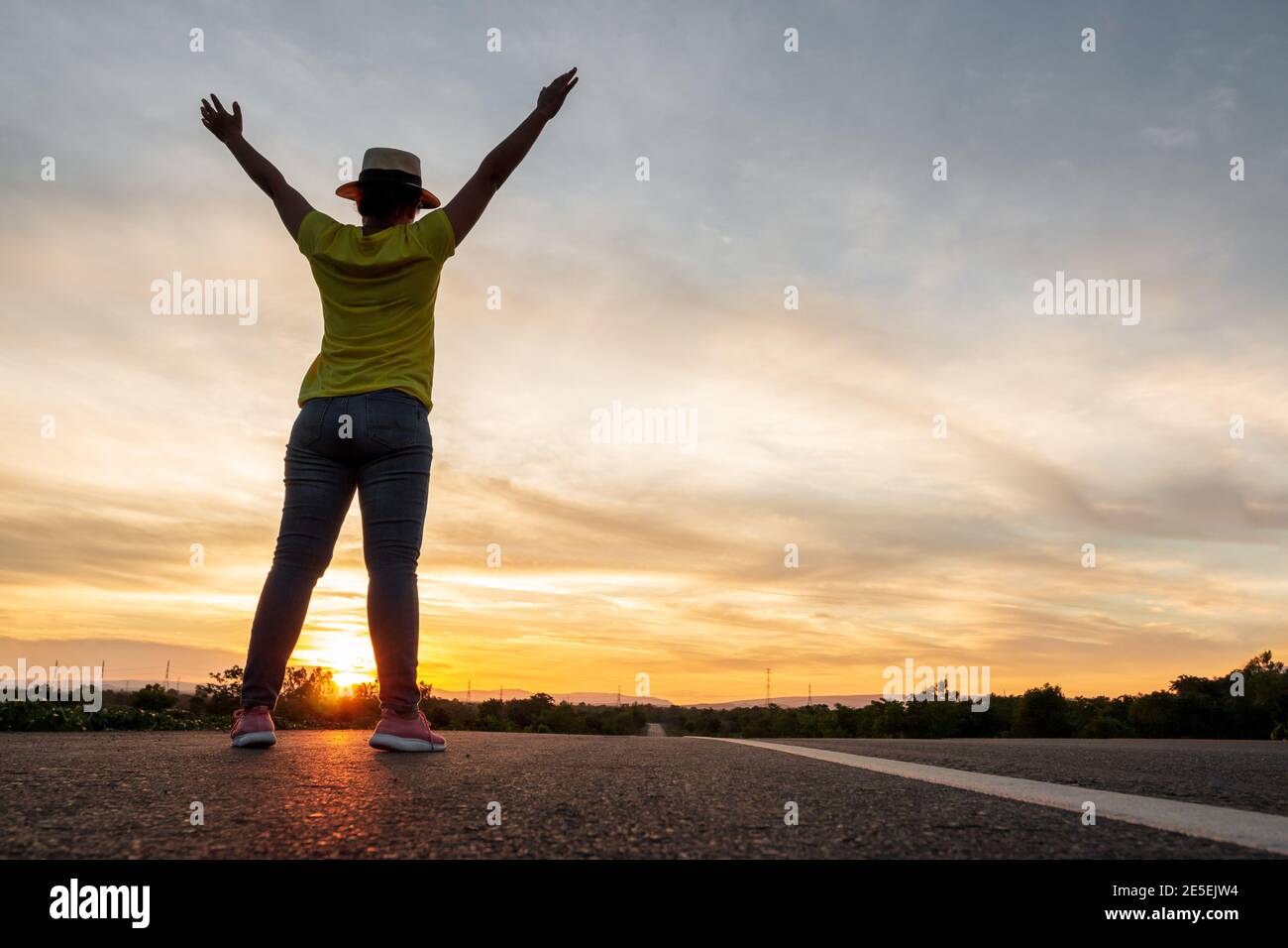 Femmes portant des tee-shirts, jeans, baskets et chapeaux au coucher du soleil, debout le long de l'autoroute pour voyager, Happy Mood, concept de vacances Banque D'Images