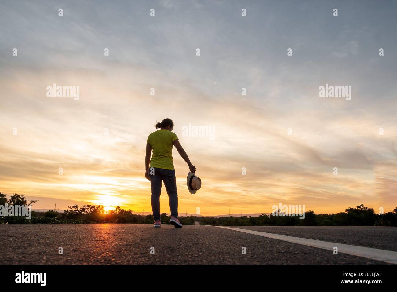 Femmes portant des tee-shirts, jeans, baskets et chapeaux au coucher du soleil, debout le long de l'autoroute pour voyager, Happy Mood, concept de vacances Banque D'Images