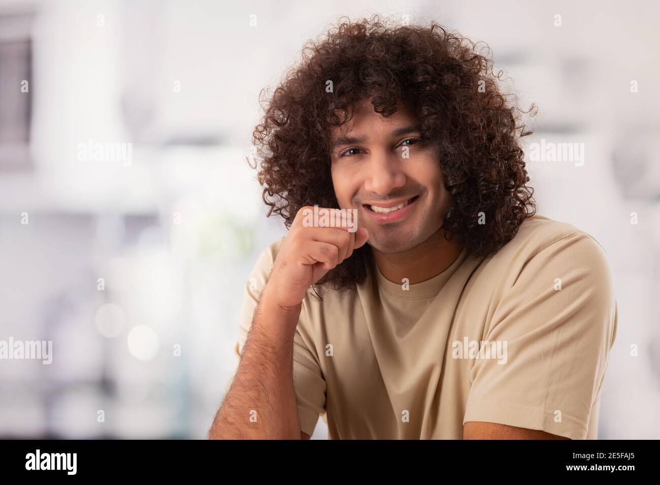 UN JEUNE HOMME HEUREUX AVEC DES CHEVEUX BOUCLÉS SOURIANT GAIEMENT À APPAREIL PHOTO Banque D'Images
