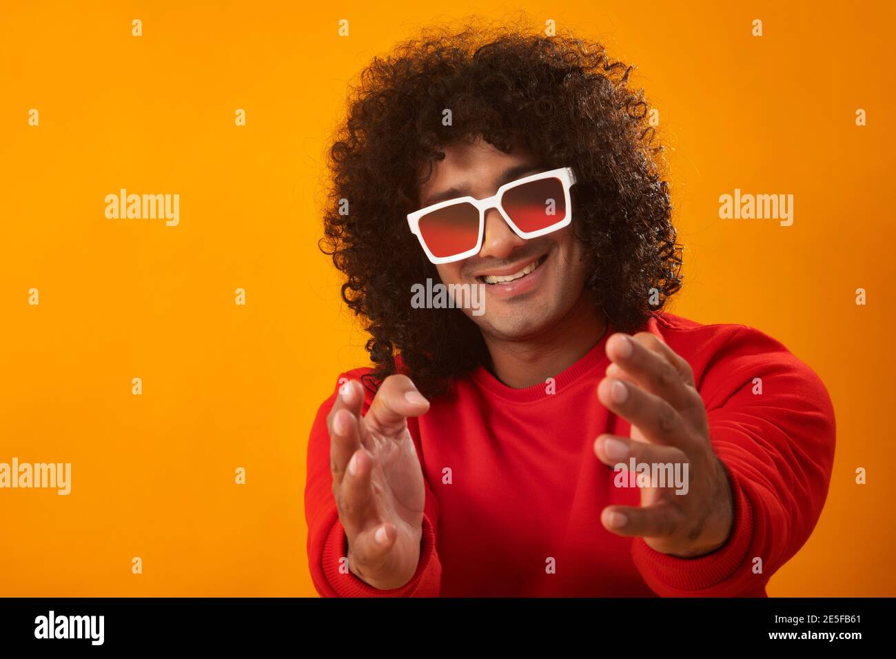 UN HOMME HEUREUX AUX CHEVEUX BOUCLÉS SE LEVANT LES MAINS VERS L'APPAREIL PHOTO ET SOURIRE Banque D'Images