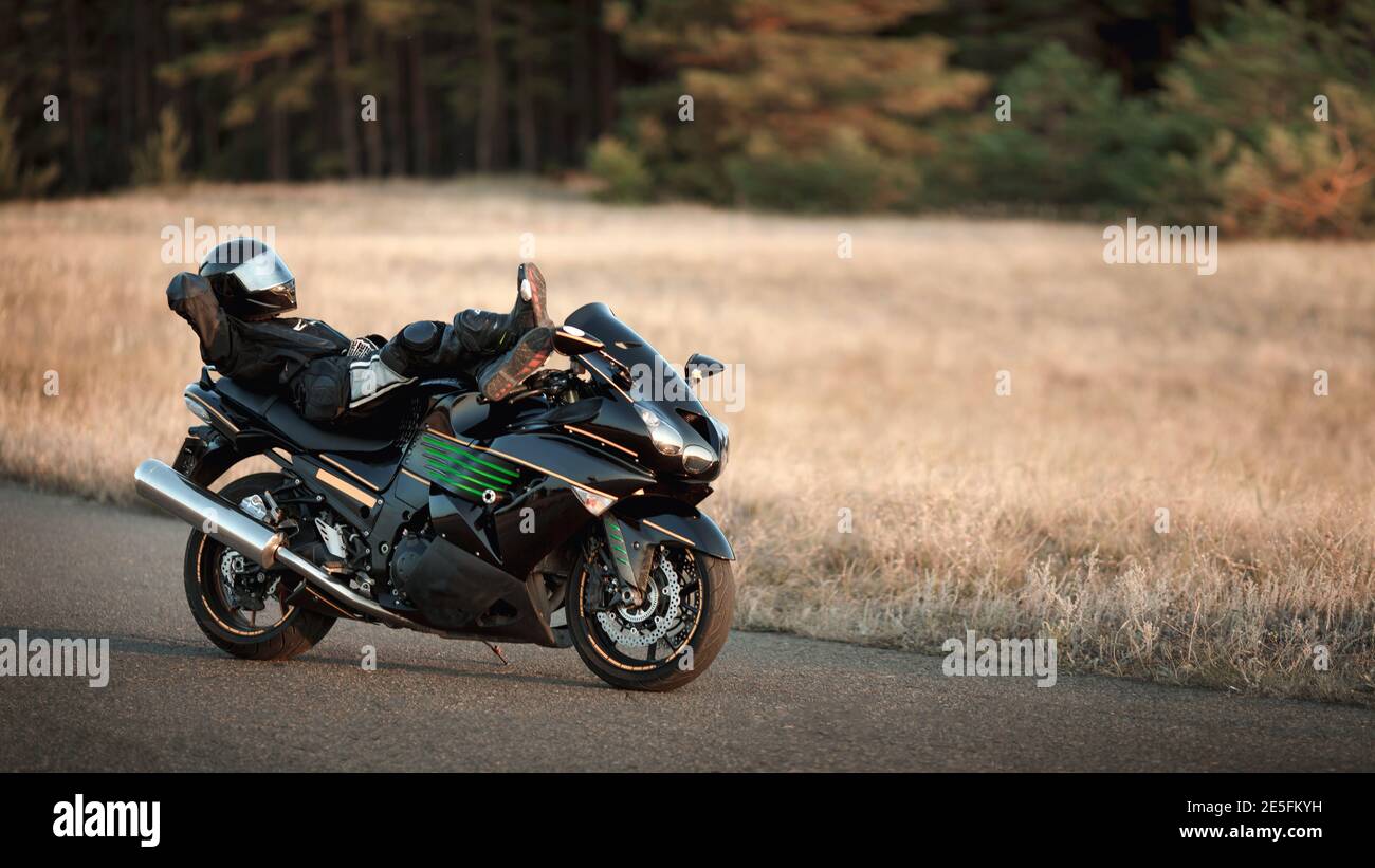 Le conducteur d'une moto en cuir se trouve sur une moto seul sur une route  asphaltée sur fond de forêt Photo Stock - Alamy