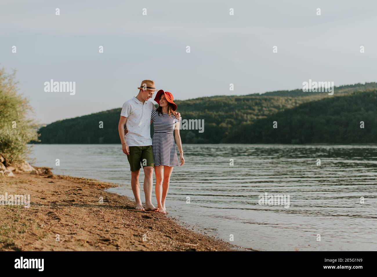 Un couple amoureux se promette le long de la plage pendant une belle soirée d'été. Portrait de la jeune femme et de l'homme qui s'embrasse tout en allant pour marcher sur l'être Banque D'Images