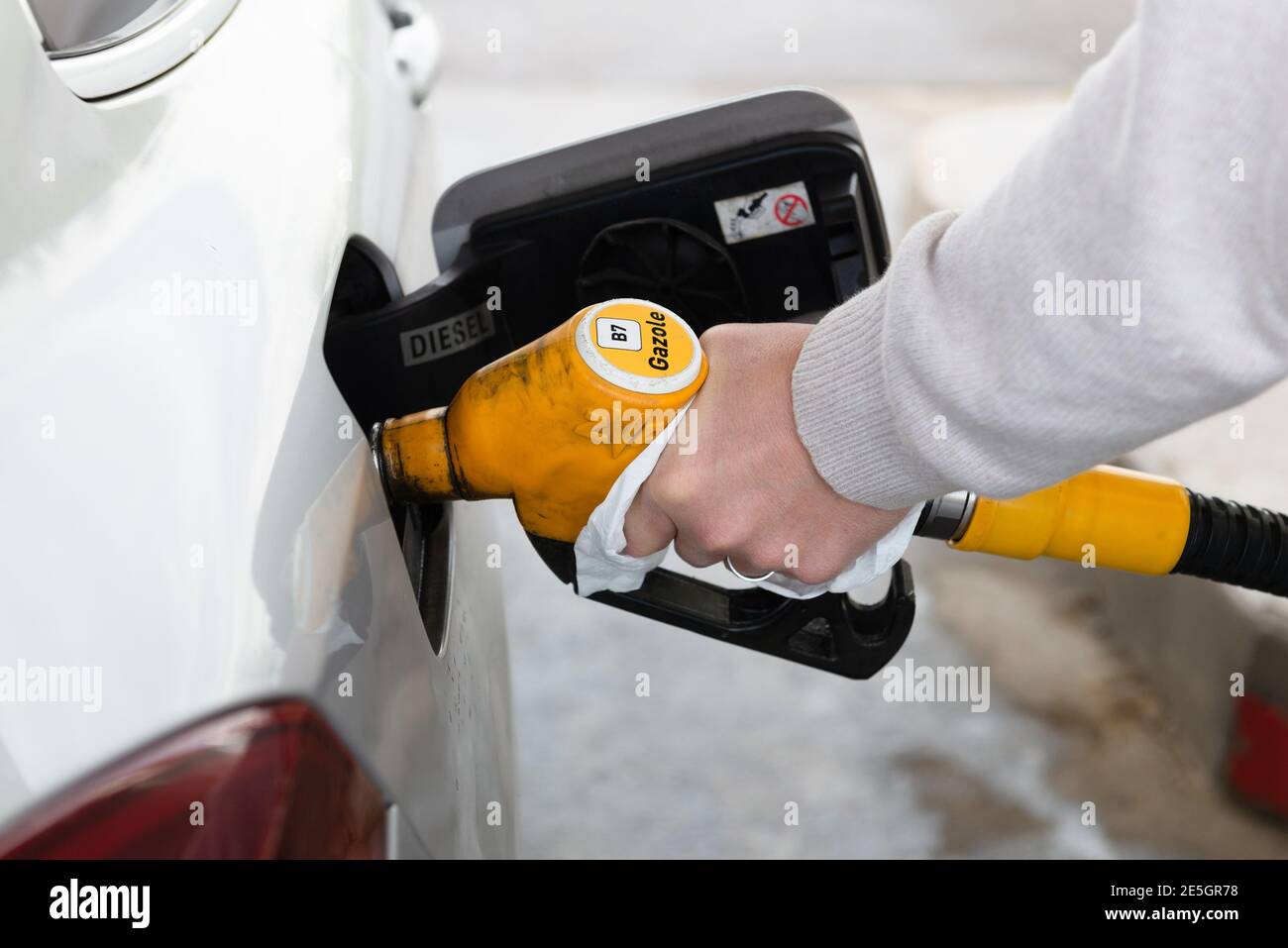 Homme manipulant avec un papier un carburant à essence jaune pompant pour faire le plein d'une voiture grise Banque D'Images