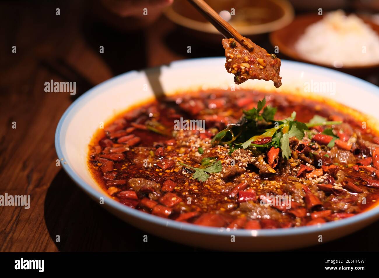 gros morceaux de baguettes ramassant les tranches de bœuf pochées dans de l'huile de chili chaude sur la table du dîner. Célèbre cuisine du Sichuan Banque D'Images