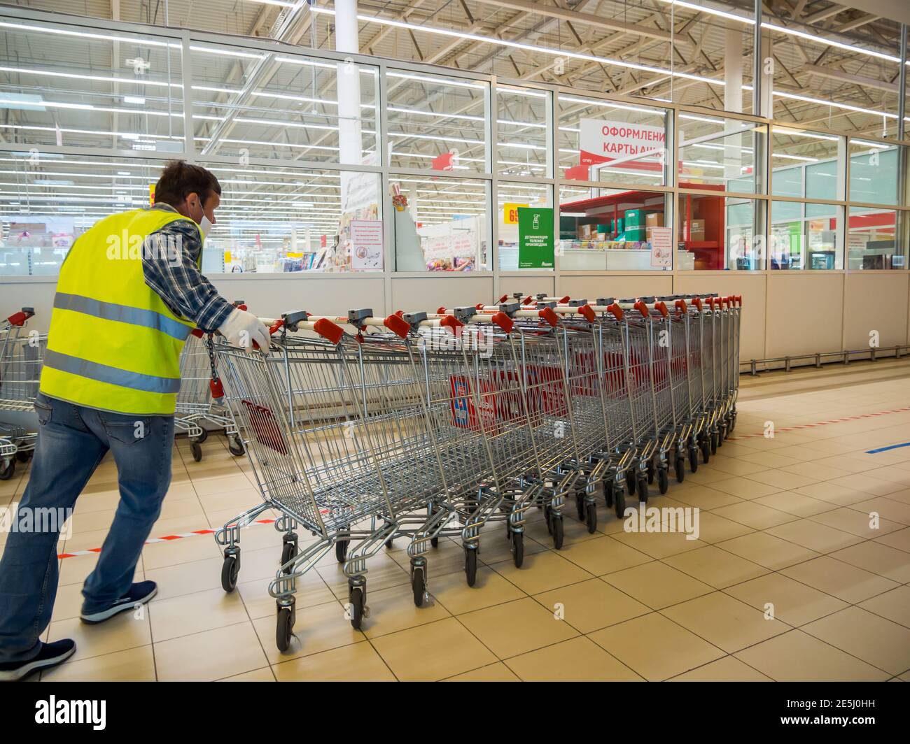 Voronezh, Russie - 13 juin 2020 : un ouvrier recueille des chariots vides au supermarché Auchan, Voronezh Banque D'Images