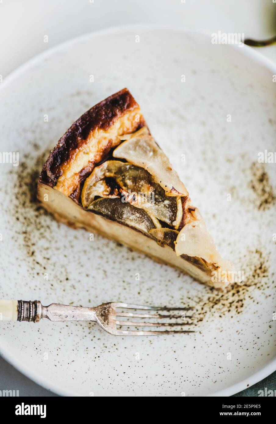 Morceau de cheesecake à la poire sans sucre végétalien sans lait dans une assiette rustique et poire fraîche sur fond de table en marbre blanc, mise au point sélective, gros plan. Concept végétarien moderne de dessert sain Banque D'Images