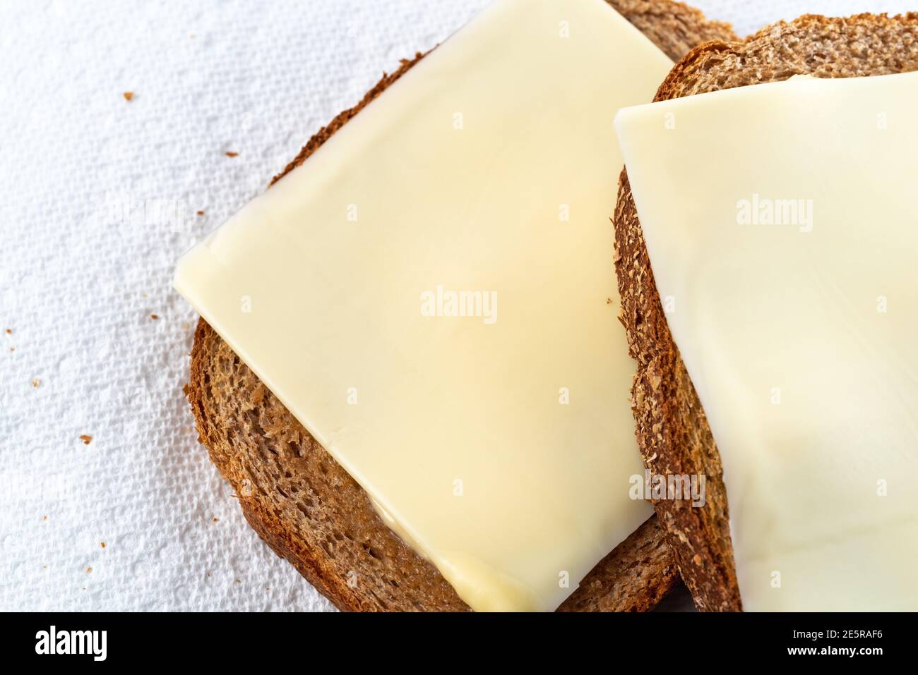 Vue rapprochée en hauteur de deux tranches de pain de blé légèrement grillé avec margarine et tranches de fromage sur des serviettes en papier blanc à la lumière naturelle. Banque D'Images