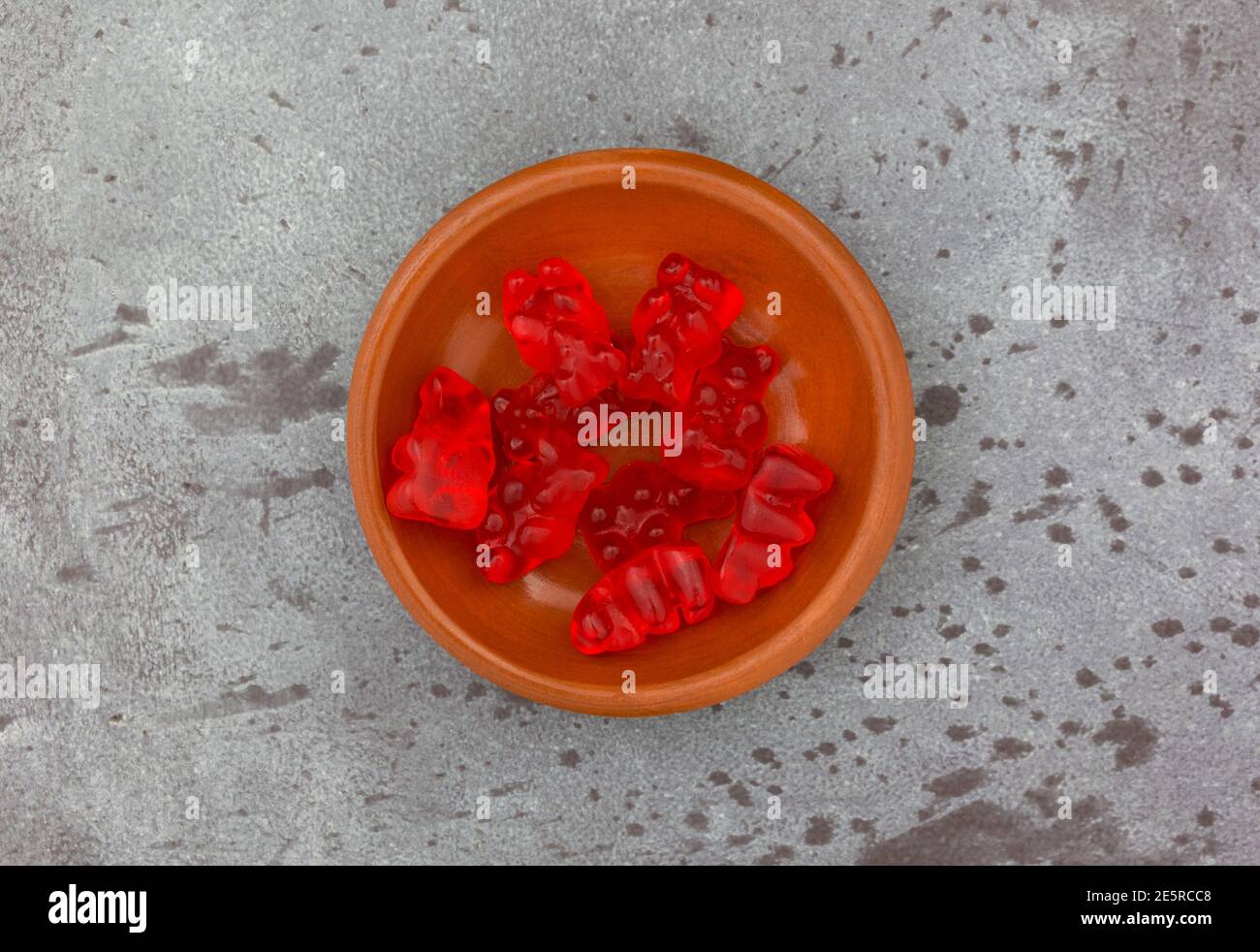 Vue en hauteur d'un petit bol de bonbons à sucre rouge gummi colorés sur un fond gris tacheté. Banque D'Images