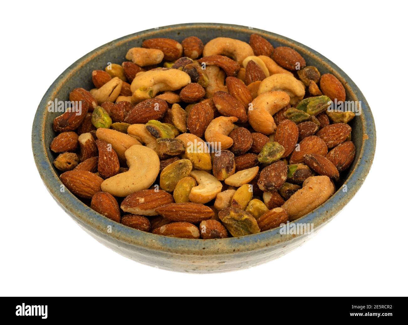 Vue latérale de pistaches, d'amandes et de noix de cajou dans un bol en grès isolé sur fond blanc. Banque D'Images