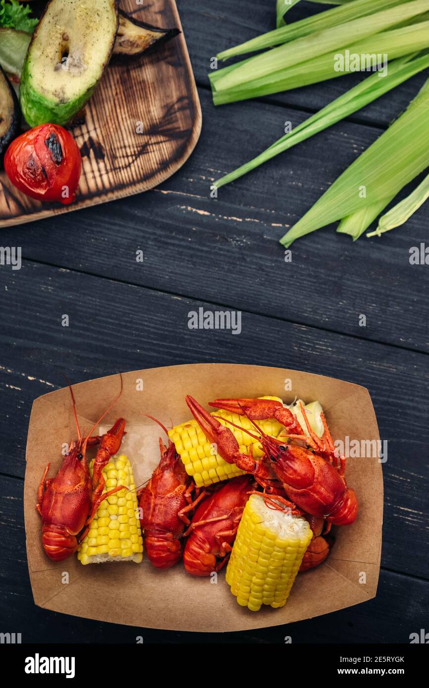 Écrevisse bouillie rouge servant avec des légumes grillés et de la verdure sur une table en bois sombre, vue du dessus Banque D'Images