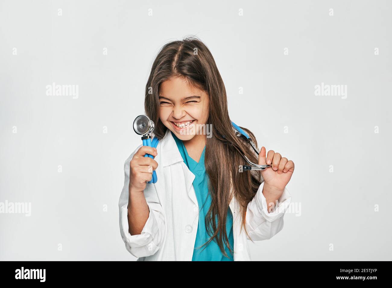 Portrait de race mixte petite fille vêtue comme un docteur avec stéthoscope dans sa main, elle pose, souriant et regardant l'appareil photo. Isolé sur blanc Banque D'Images