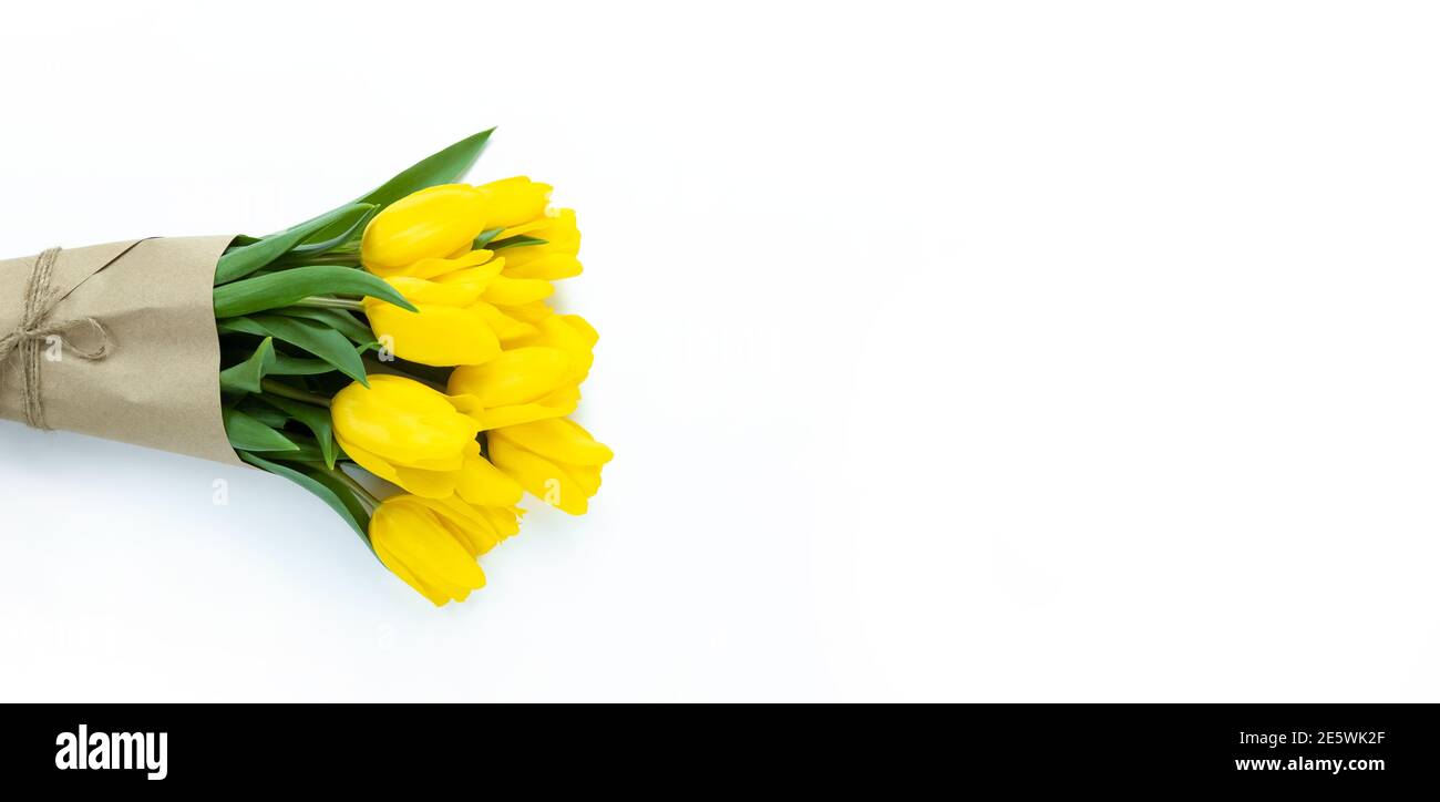 Bouquet de tulipes jaunes enveloppées de papier artisanal sur fond blanc avec espace de copie. Banque D'Images