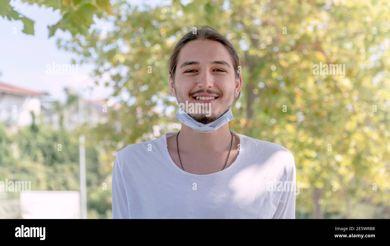 Portrait d'un jeune homme souriant beau dans un masque médical. Son masque est sous le menton. Nouvelle normalité après la pandémie de Covid-19. Banque D'Images