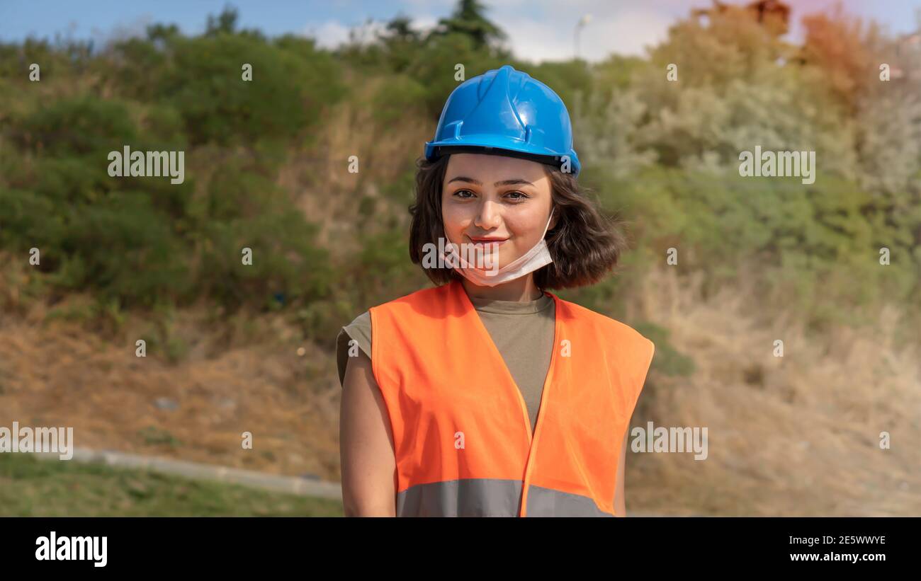 Portrait d'une jeune femme gaie ingénieur ou travailleur dans un casque de protection bleu uniforme, souriant et regardant la caméra sur le chantier Banque D'Images