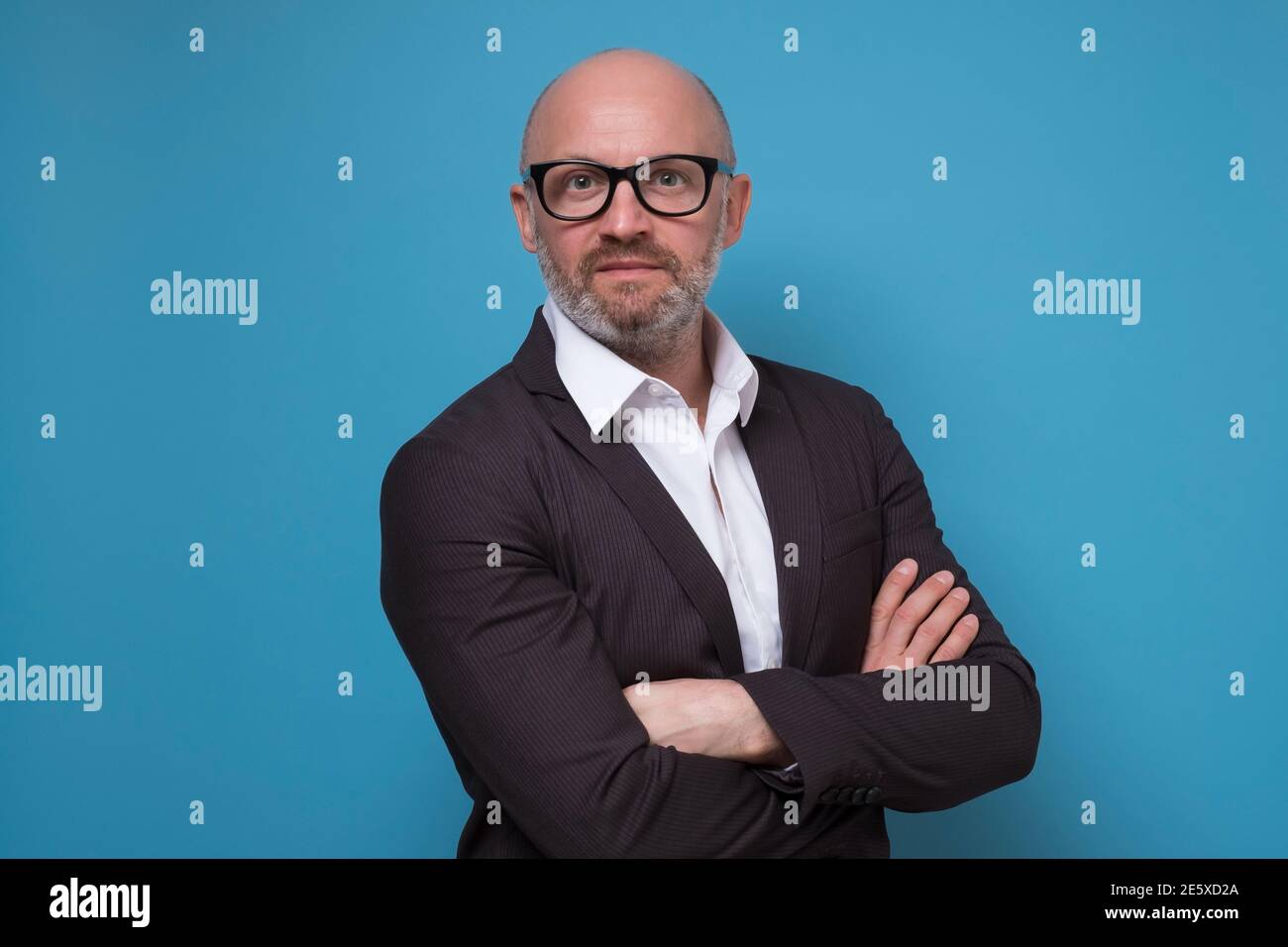 Beau homme d'affaires mature en costume debout avec les bras croisés arrière-plan bleu Banque D'Images