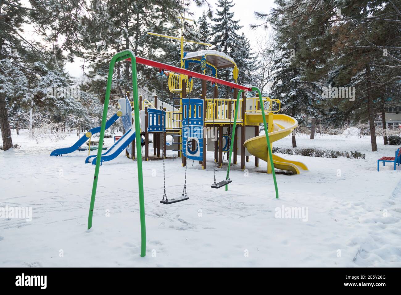 Le terrain de jeu coloré est recouvert de neige en hiver. Au premier plan se trouvent les balançoires. Banque D'Images