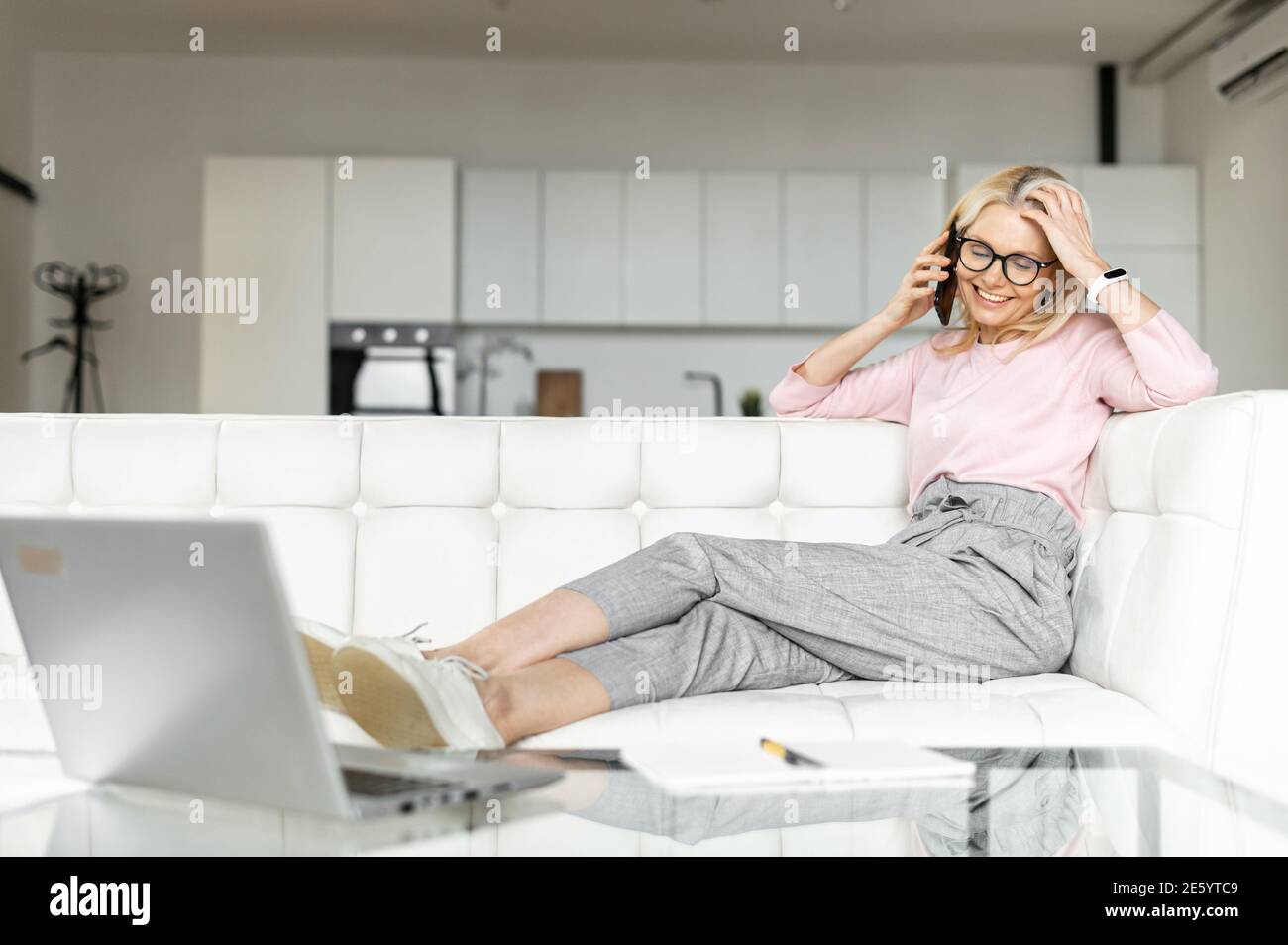 Charmante femme d'âge moyen a une conversation téléphonique, une femme d'affaires détendue se pose sur le canapé, regarde vers le bas, rire et bavarder sur le smartphone tout en Banque D'Images