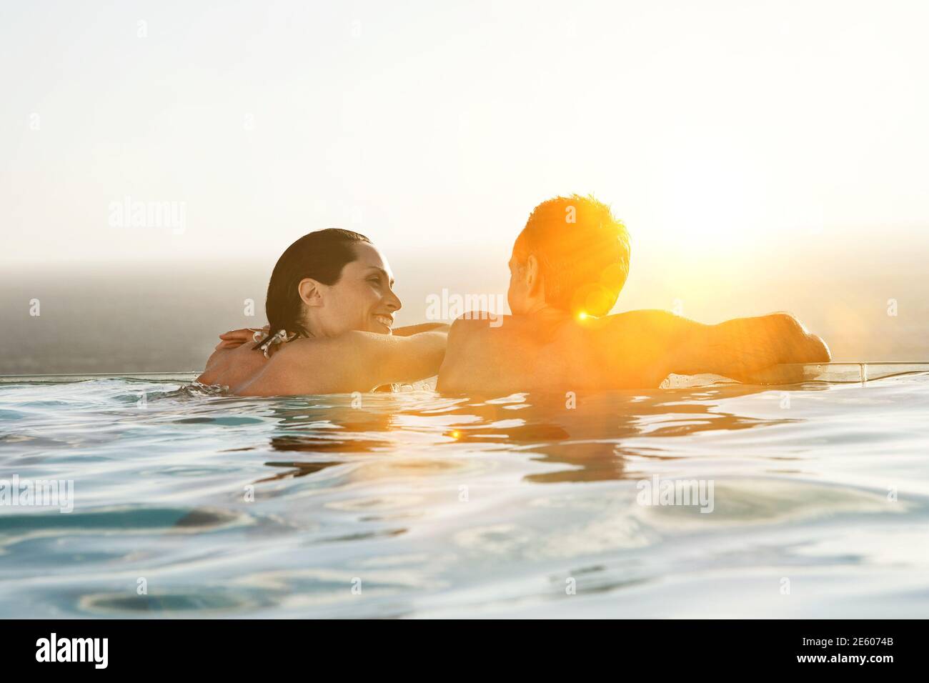 Vue arrière du couple se détendre dans la piscine à débordement du complexe Banque D'Images