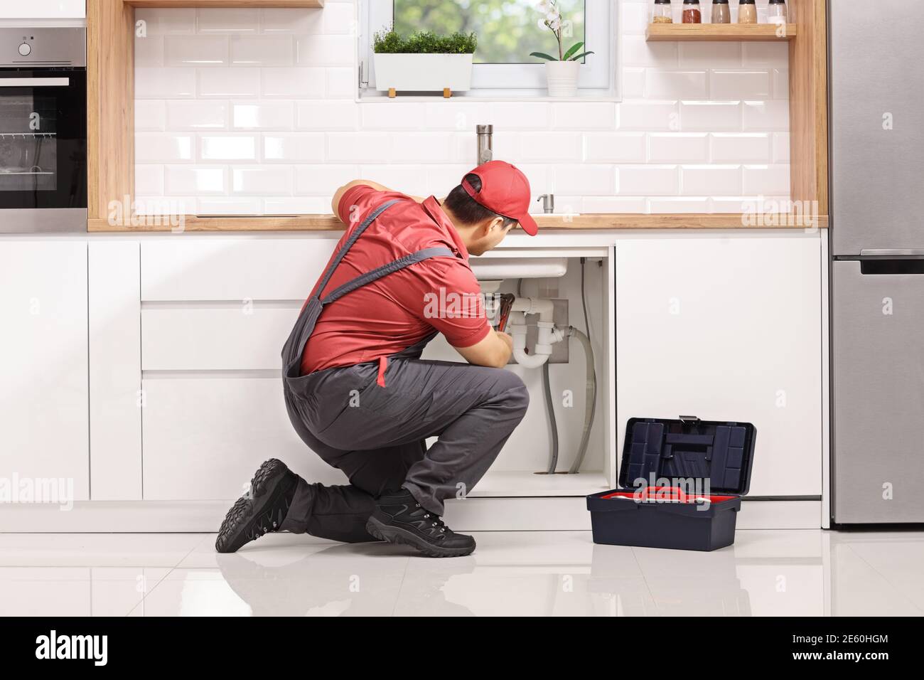 Plomber agenouiller et fixer un tuyau sous l'évier dans un cuisine moderne Banque D'Images